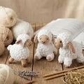 Three knitted sheep figurines on a wooden table with yarn and needles nearby