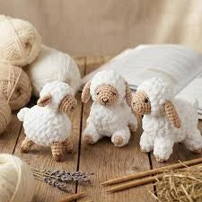 Three knitted sheep figurines on a wooden table with yarn and needles nearby